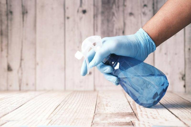 A gloved hand holding a spray bottle on a wooden surface